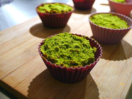 Wytrawne muffinki z zielonego groszku w czerwonych silikonowych foremkach na drewnianej desce