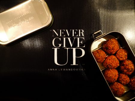 Kulki z daktyli, jagód goji i wiórków kokosowych ułożone w metalowym lunchboxie Anny Lewandowskiej z napisem Never Give Up.