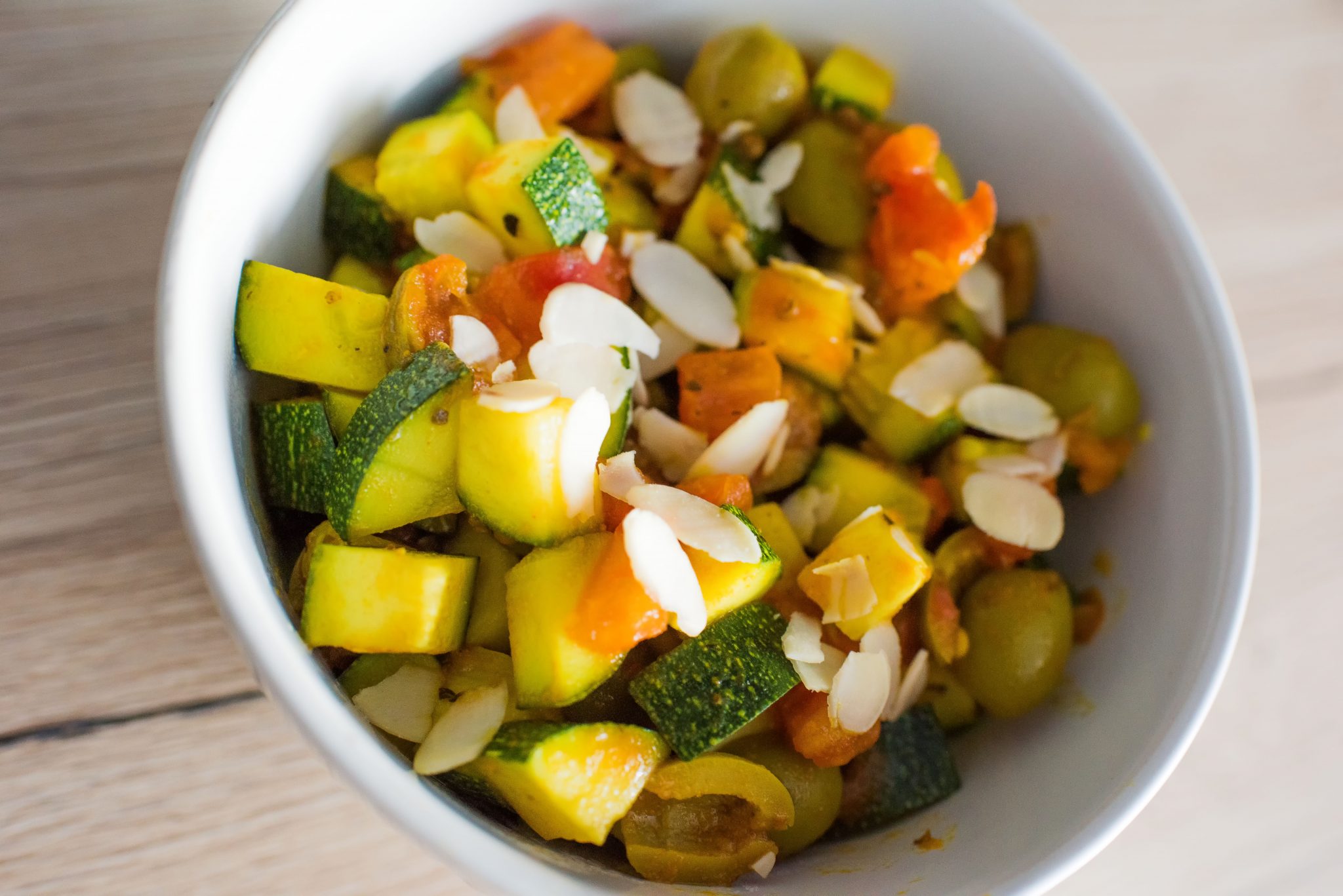 Duszone warzywa z cukinią, marchewką i płatkami migdałów w białej misce