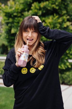 Anna Lewandowska pije owsiankę do picia ze szklanej butelki przez słomkę, w ogrodzie