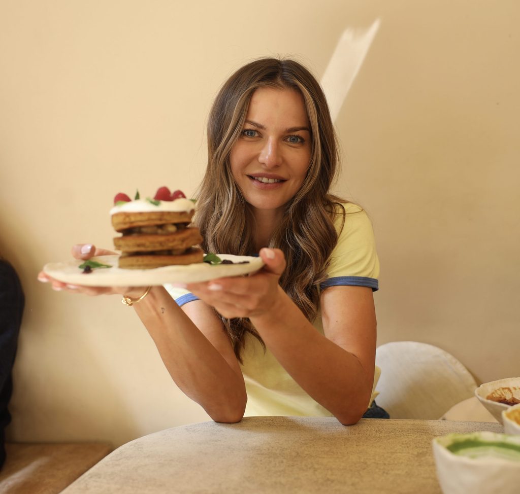 Anna Lewandowska holding a layered cake topped with strawberries on a wooden board