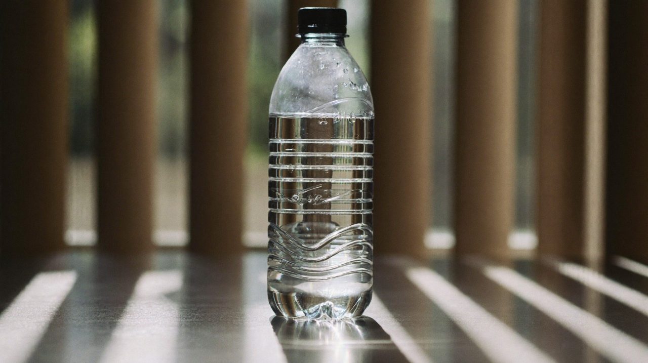 A plastic bottle of water standing on a wooden surface in the sun